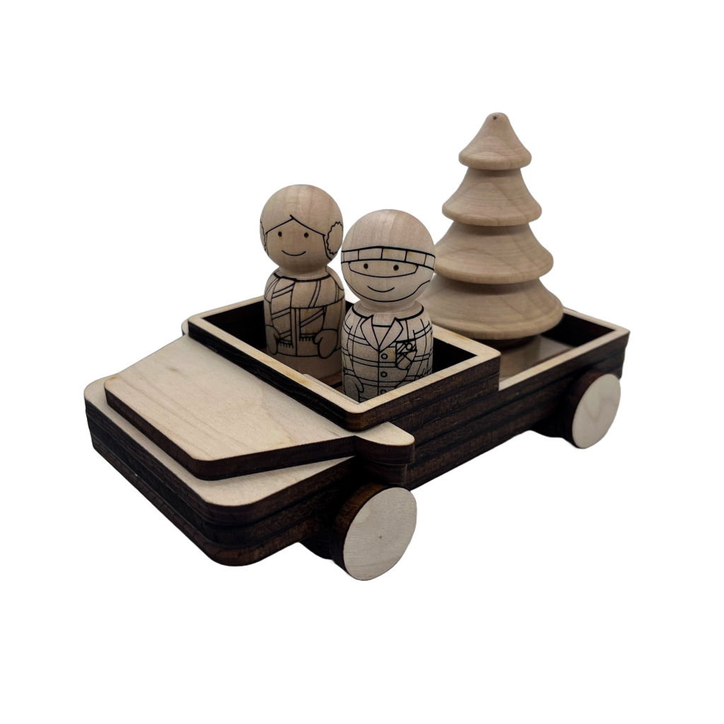 Boy and girl peg doll characters riding in a wooden pickup truck with wooden christmas tree in the truck bed.