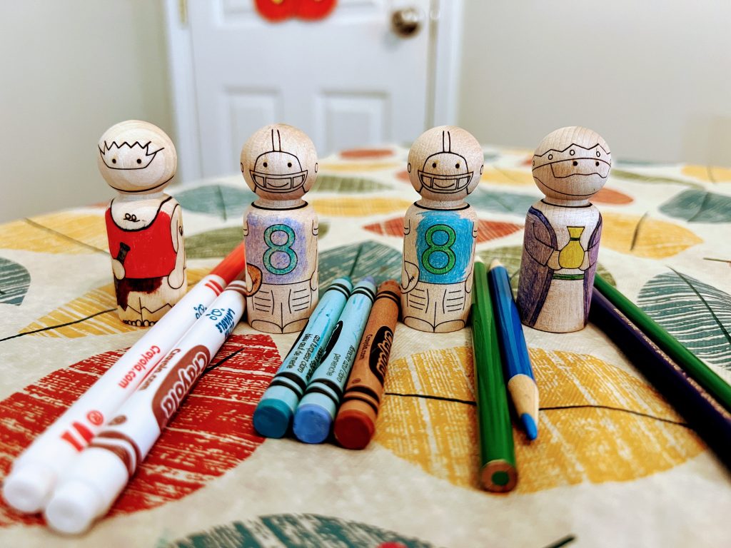 wooden peg dolls laser engraved to look like a pirate, football player, and king all colored with various mediums: marker, crayon, and pencil