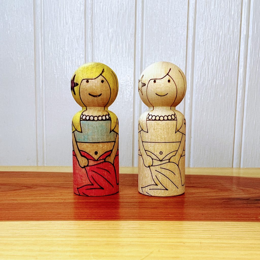Wooden peg doll that is laser engraved to look like a mermaid. Side by side color pencil finished and one unfinished.